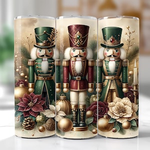 May include: Three tumblers with a Christmas nutcracker design. The tumblers feature illustrations of nutcrackers in green and burgundy uniforms, with white hair and mustaches. The background includes Christmas ornaments, poinsettias, and pine needles.