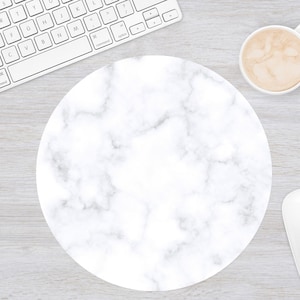 May include: A round white marble-patterned mousepad with a white computer mouse, a white keyboard, and a cup of coffee on a light wood-grain surface. The mousepad has a smooth, polished appearance.
