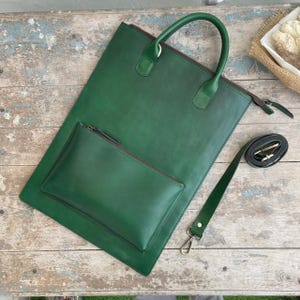 May include: A green leather tote bag with a matching pouch and a detachable shoulder strap. The tote has a top handle and a zip closure. The pouch is attached to the front. The strap is black with silver hardware.