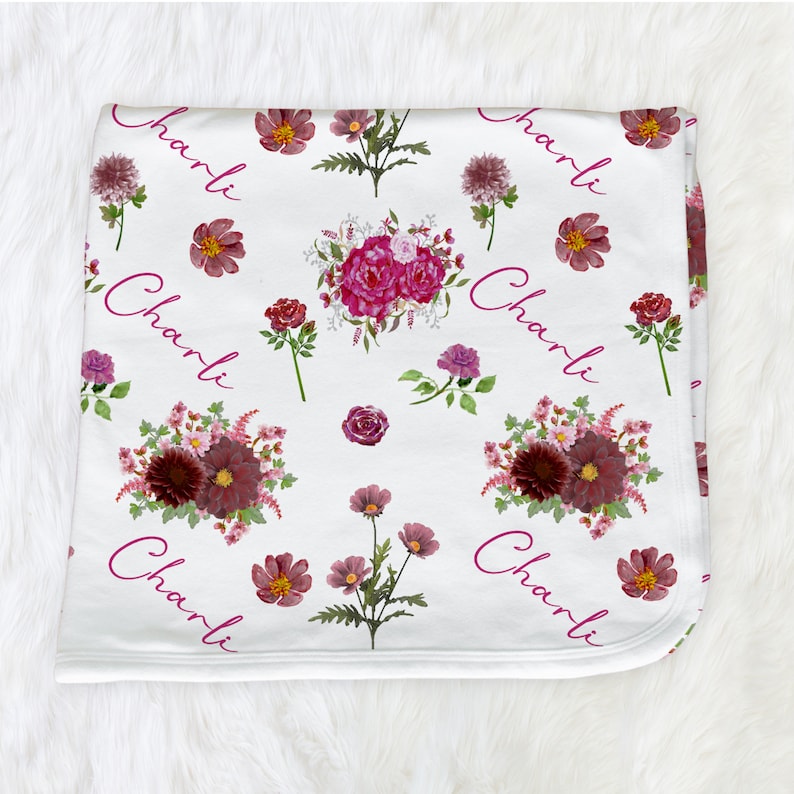 Puede incluir: Manta de beb&eacute; blanca con un patr&oacute;n floral en tonos rosa y burdeos. La manta tiene el nombre "Charli" repetido en todo el dise&ntilde;o.