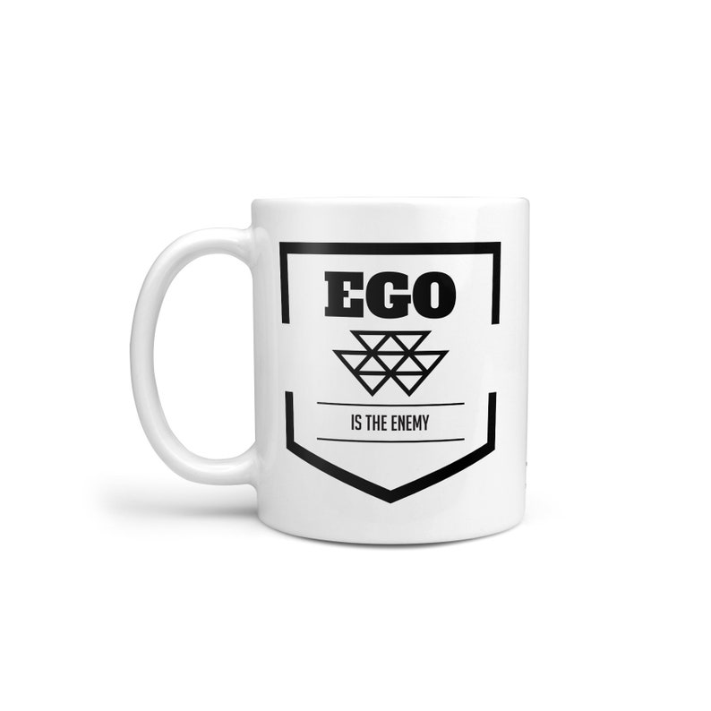 May include: White ceramic mug with a black graphic design. The design features a shield with the word "EGO" in all caps and the text "IS THE ENEMY" below it.