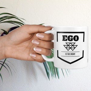 May include: White ceramic mug with a black graphic that says "Ego is the enemy".