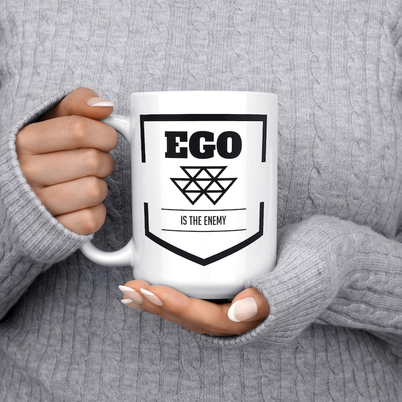 May include: White ceramic mug with a black graphic that says "EGO IS THE ENEMY" with a geometric design.