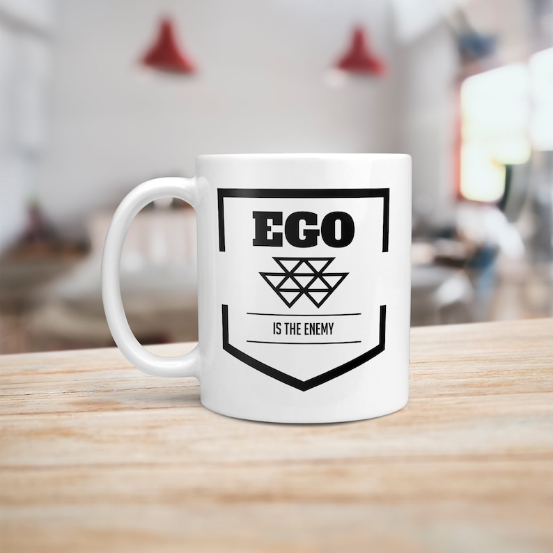May include: White ceramic mug with a black graphic that says "Ego is the enemy". The graphic features a black geometric design.