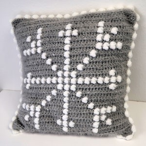 May include: Gray and white crocheted throw pillow with a snowflake design. The pillow has a fluffy texture and a white border.