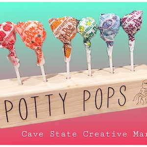 May include: Wooden stand with the words "Potty Pops" engraved on the front. The stand has six holes to hold lollipops. The lollipops are wrapped in colorful paper with different flavors, including strawberry, orange, scotch butter, cream soda, and grape.