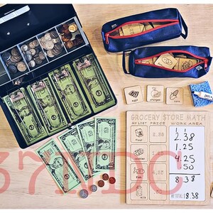 May include: A wooden board with the words "Grocery Store Math" written on it. There are several sections labeled "My List Price" and "Work Area". The board has a white dry-erase surface with handwritten numbers and a total of 8.38. There are also several wooden squares with numbers written on them, a cash register with play money, and two blue zippered pouches with wooden squares inside.