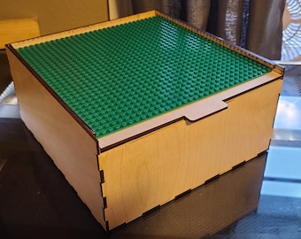 May include: A wooden box with a green Lego base plate lid. The box is made of light wood and has a hinged lid.