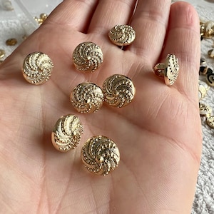 May include: Eight gold-toned buttons with a swirl design. The buttons are round and have a raised, textured surface.