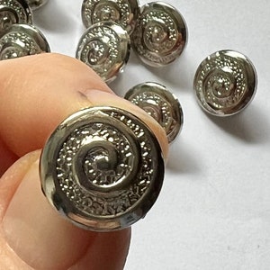 May include: Silver metal buttons with a spiral design. The buttons are round and have a raised edge.