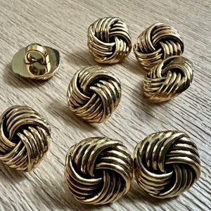 May include: Eight gold-toned buttons with a knotted design. The buttons are round and have a raised, textured surface.