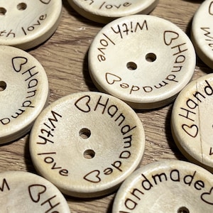 May include: A collection of wooden buttons with the text "Handmade with love" and a heart symbol. The buttons are light brown and have two holes.