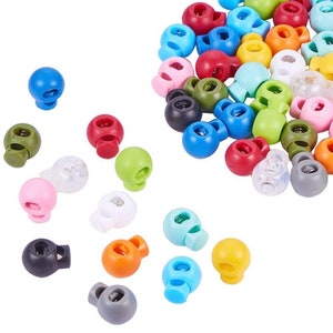 May include: A selection of multi-coloured cord locks, featuring shades of blue, red, green, and yellow. These small plastic toggles are designed for adjusting cords and drawstrings, with a round body and a spring-loaded mechanism.