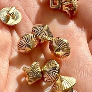 May include: A collection of gold-toned metal buttons with a pyramid shape and a decorative, ribbed design. The buttons have a variety of sizes and styles.