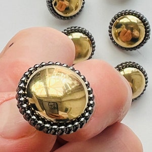 May include: A set of six gold-toned buttons with a black beaded trim. The buttons are round and have a raised, domed centre.