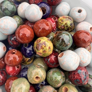 May include: A selection of ceramic beads in shades of red, green, blue, and white. The beads are glazed and have a hole for threading. Some beads feature speckled designs and a glossy finish.