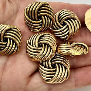 May include: Six gold-toned metal buttons with a woven knot design. The buttons are round and have a raised, textured surface.