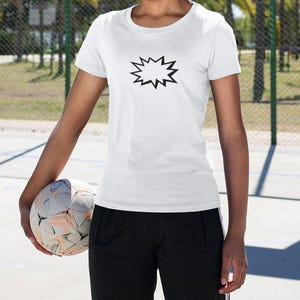 Könnte beinhalten: Weißes T-Shirt mit Rundhalsausschnitt und schwarzem Stern-Burst-Grafik. Die Person hält einen Fußball und trägt eine schwarze Sporthose. Der Hintergrund umfasst einen Maschendrahtzaun und Palmen.