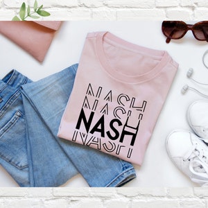 Puede incluir: Una camiseta rosa con la palabra "NASH" repetida en una fuente geom&eacute;trica negra.
