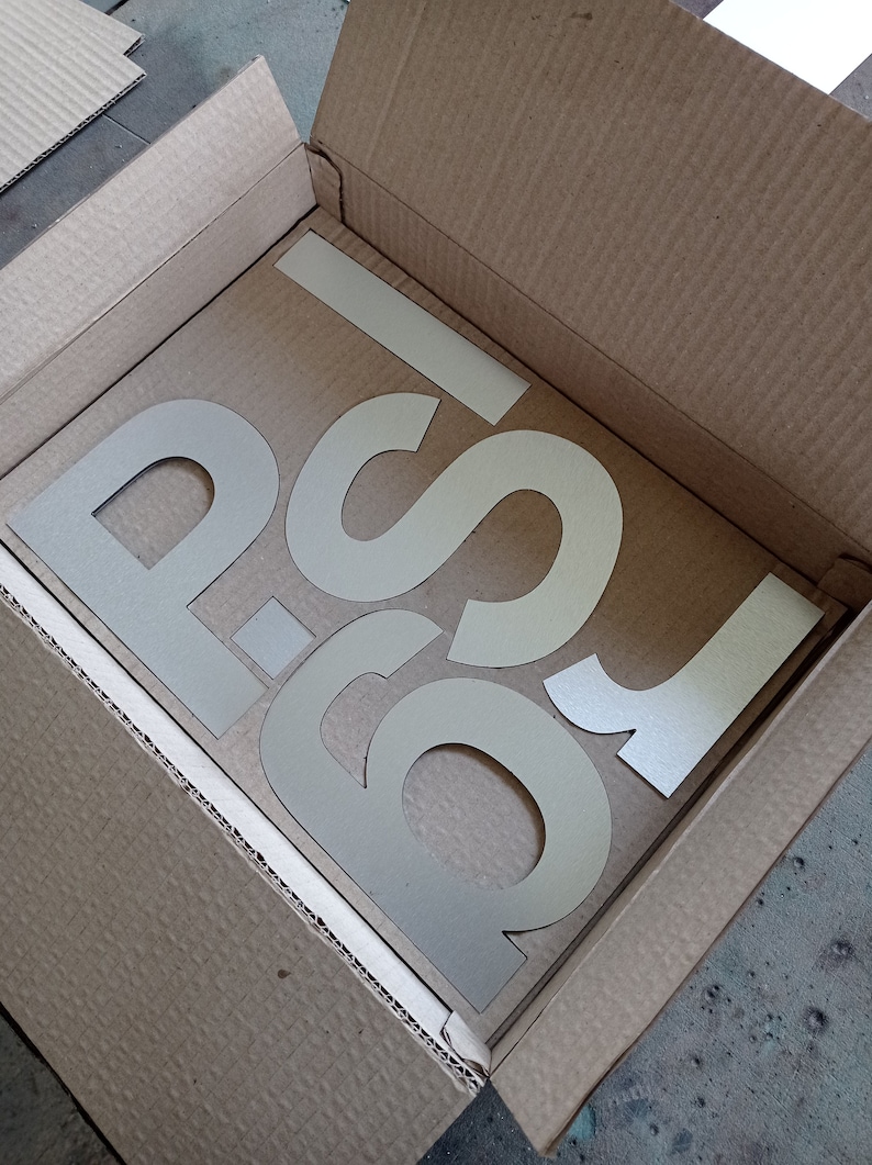 Puede incluir: Una caja de cart&oacute;n con las letras "P-S" recortadas en el cart&oacute;n. Las letras son de color beige claro.