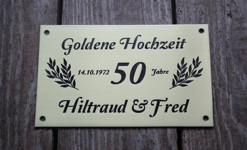 May include: A gold-colored metal plaque with black lettering. The plaque reads "Goldene Hochzeit" with the date "14.10.1972" and the number "50" followed by the word "Jahre". The plaque also reads "Hiltraud & Fred".