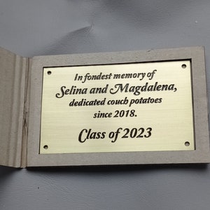 May include: A gold plaque with the inscription "In fondest memory of Selina and Magdalena, dedicated couch potatoes since 2018. Class of 2023".