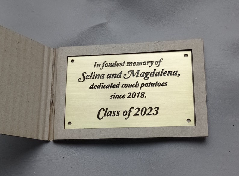 May include: A gold plaque with the inscription "In fondest memory of Selina and Magdalena, dedicated couch potatoes since 2018. Class of 2023".