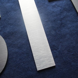 Puede incluir: Primer plano de tres letras de metal plateado cepillado, la primera letra es una 'S', la segunda letra es una 'I' y la tercera letra es una 'T'. Las letras est&aacute;n sobre un fondo azul oscuro.