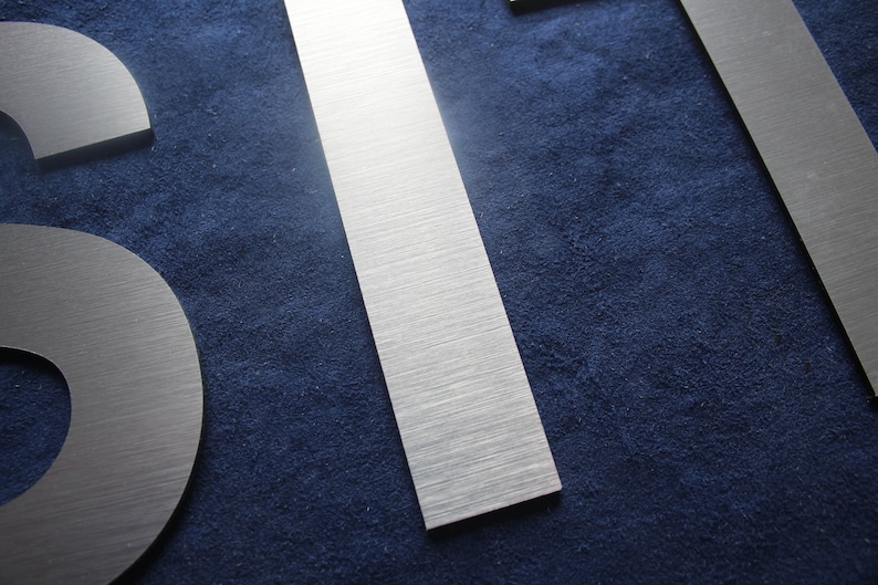 Puede incluir: Primer plano de tres letras de metal plateado cepillado, la primera letra es una 'S', la segunda letra es una 'I' y la tercera letra es una 'T'. Las letras est&aacute;n sobre un fondo azul oscuro.