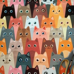 May include: A colorful fabric with a repeating pattern of cartoon cats. The cats are in various poses and colors, including black, white, brown, orange, red, pink, and blue.