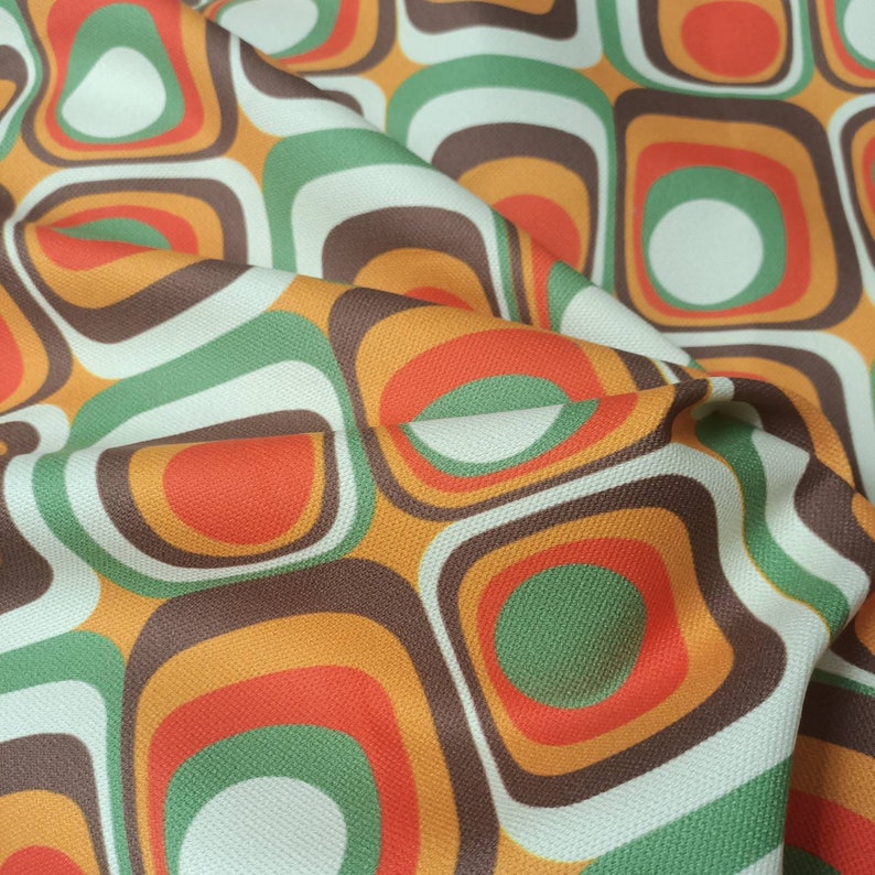 May include: A fabric with a retro pattern of overlapping circles and squares in shades of orange, brown, green, and white.