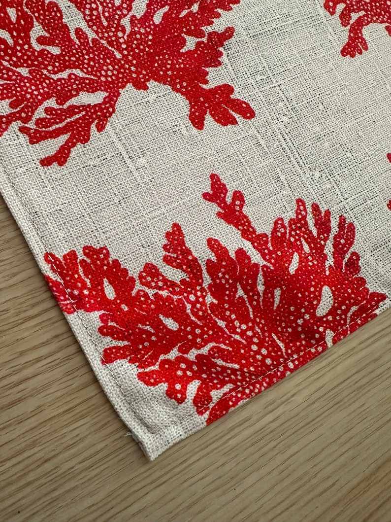 May include: A white fabric placemat with a red coral design. The placemat has a stitched edge.