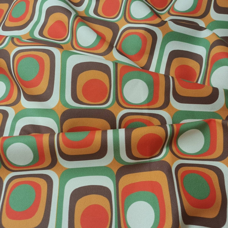 May include: A fabric with a repeating pattern of squares and circles in shades of brown, orange, green, and white.