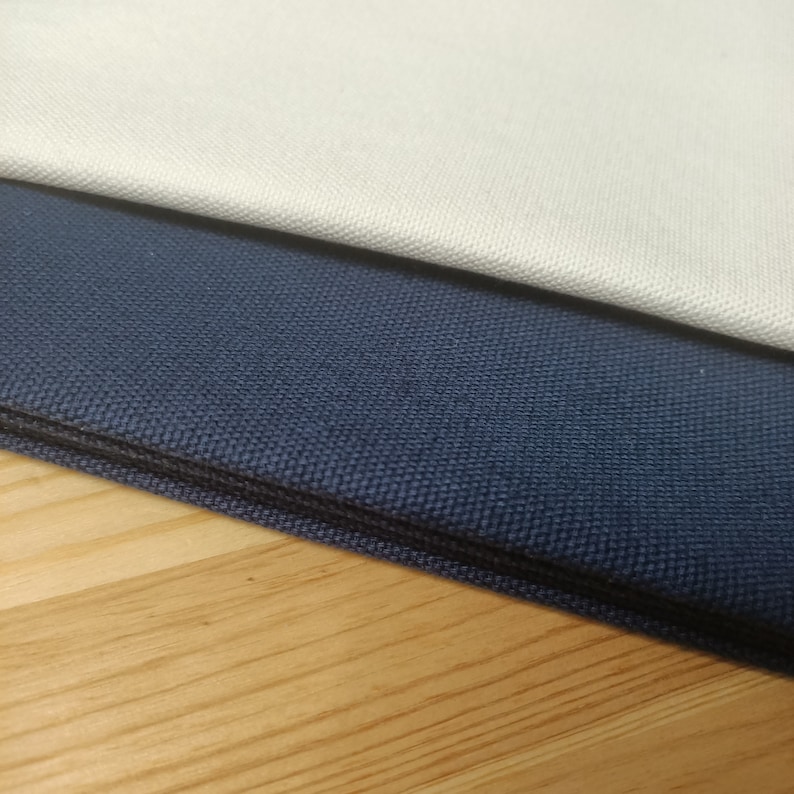 Puede incluir: Dos muestras de tela, una de color beige claro y la otra de color azul marino oscuro. Las muestras est&aacute;n dobladas y superpuestas.