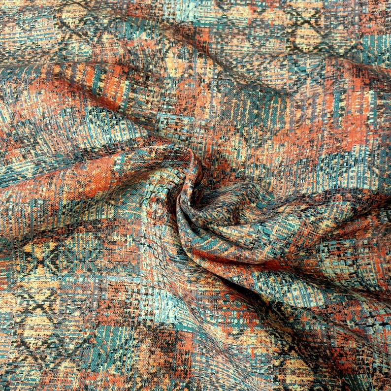 May include: A close-up of a fabric with a textured, abstract pattern in shades of orange, blue, and brown.