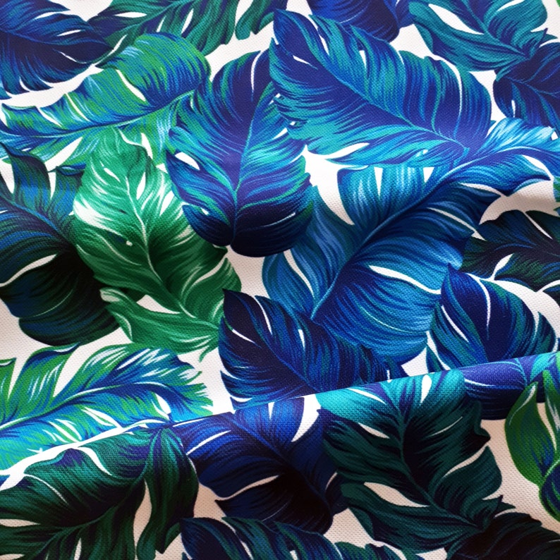 May include: A close-up of a fabric with a tropical leaf pattern. The leaves are in shades of blue and green, with white spaces between them. The leaves have a detailed vein structure.
