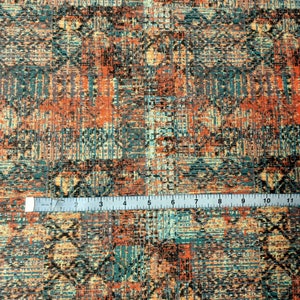 May include: A close-up of a fabric with a colorful, abstract pattern. The fabric is a mix of orange, blue, and brown colors, and has a textured, woven look. A ruler is placed on top of the fabric, showing the scale.