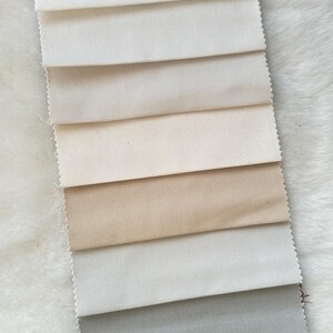 Puede incluir: Una colecci&oacute;n de muestras de tela en varios tonos de blanco, beige, gris y rojo. Las muestras est&aacute;n dispuestas en una pila vertical, con el tono m&aacute;s claro en la parte superior y el tono m&aacute;s oscuro en la parte inferior.