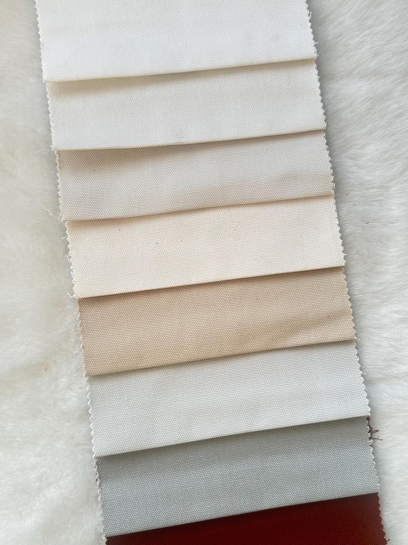 Puede incluir: Una colecci&oacute;n de muestras de tela en varios tonos de blanco, beige, gris y rojo. Las muestras est&aacute;n dispuestas en una pila vertical, con el tono m&aacute;s claro en la parte superior y el tono m&aacute;s oscuro en la parte inferior.