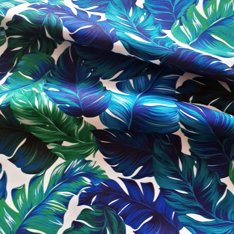 May include: Fabric with a tropical leaf pattern in shades of blue and green. The leaves have a detailed vein structure and are set against a white background. The fabric has a slight sheen and a soft texture.