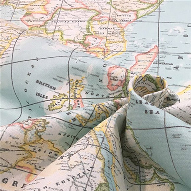 Puede incluir: Primer plano de una tela con un dise&ntilde;o de mapa del mundo vintage. El mapa presenta continentes en tonos beige, amarillo y rosa, con oc&eacute;anos azules y l&iacute;neas de cuadr&iacute;cula negras. La tela est&aacute; doblada, mostrando los intrincados detalles del mapa.