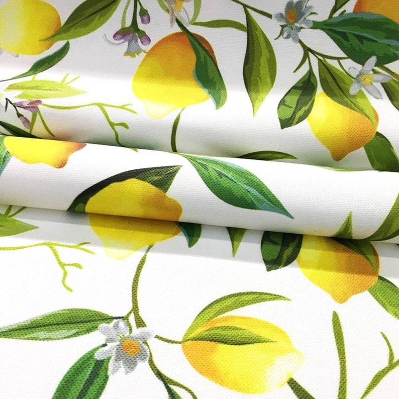 May include: White fabric with a repeating pattern of yellow lemons and green leaves. The lemons are arranged in a diagonal pattern and the leaves are arranged in a vertical pattern.