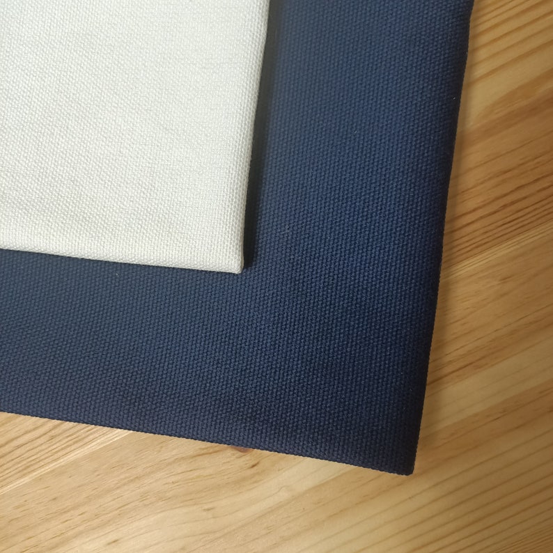 Puede incluir: Dos muestras de tela, una blanca y otra azul oscuro, se colocan sobre una superficie de madera clara. Las muestras son texturizadas y parecen estar hechas de lona.