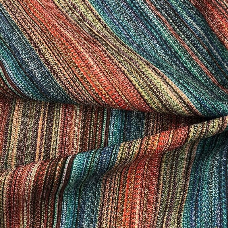 May include: Close-up of a colorful fabric with a striped pattern. The fabric features a blend of colors, including red, orange, teal, blue, and brown. The stripes run diagonally across the material, creating a textured appearance.