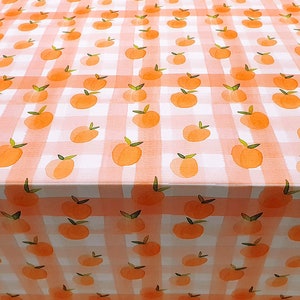 May include: A white tablecloth with a pink and white gingham pattern and a peach design. The tablecloth is covered in peach illustrations.
