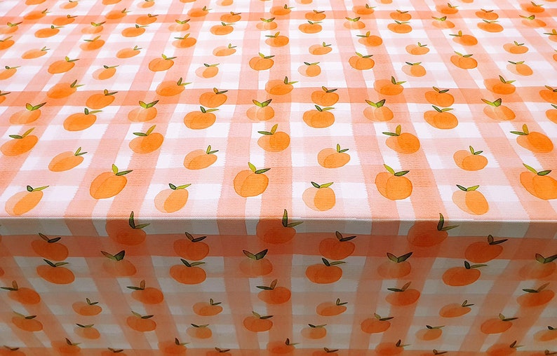 May include: A white tablecloth with a pink and white gingham pattern and a peach design. The tablecloth is covered in peach illustrations.