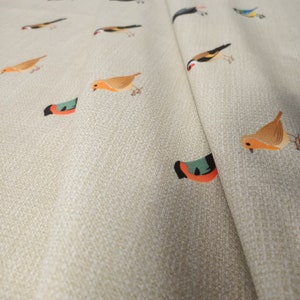 May include: Beige fabric with a repeating pattern of colorful birds. The birds are in various poses, including flying, perched, and singing.