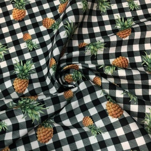 Op de afbeelding: Zwart-wit gingham stof met een herhalend patroon van groene ananas. De ananas zijn in een realistische stijl geprint.