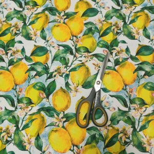 May include: A white fabric with a repeating pattern of yellow lemons and green leaves. The fabric is accented with a pair of silver scissors.