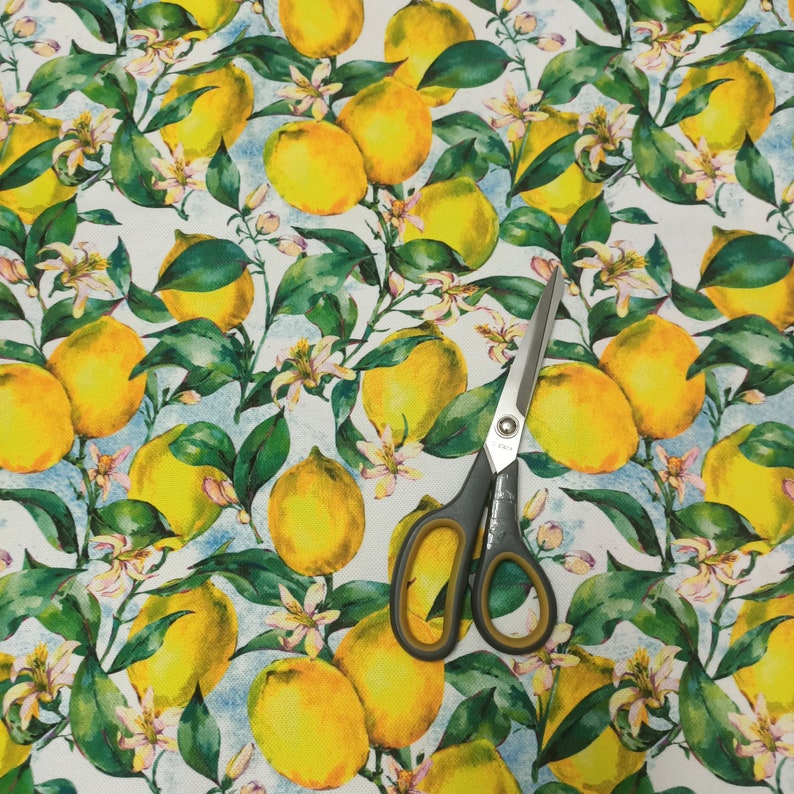 May include: A white fabric with a repeating pattern of yellow lemons and green leaves. The fabric is accented with a pair of silver scissors.